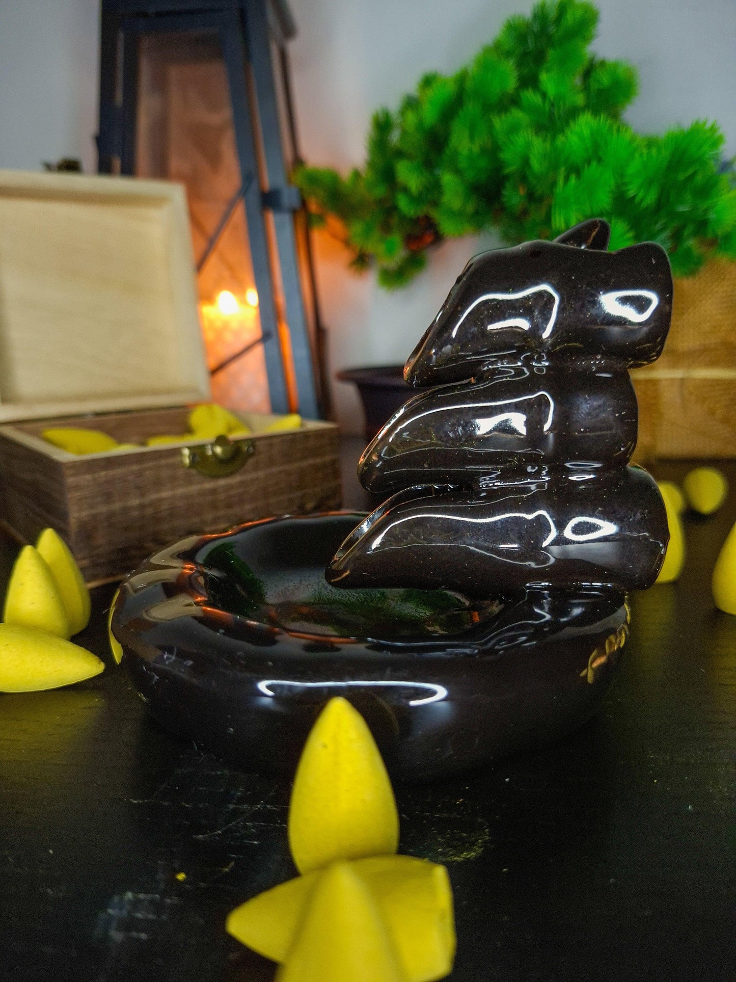 Ceramic backflow incense burner with yellow incense cones, wooden box, and candle lantern